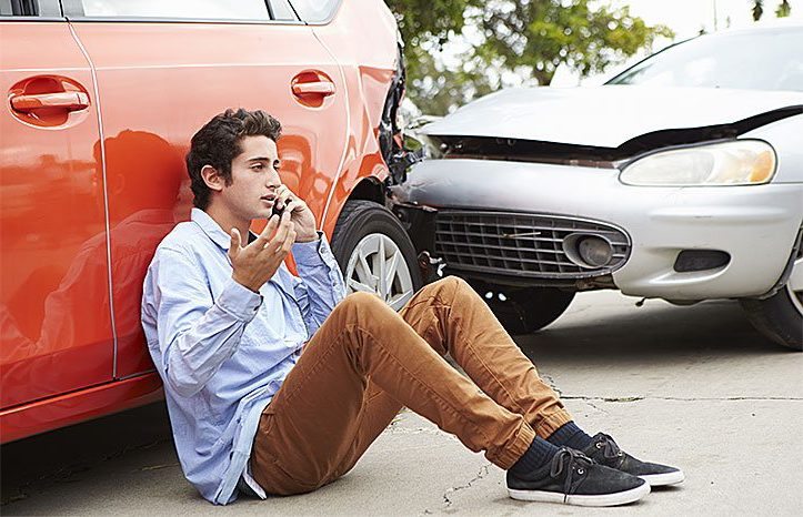 Young driver on a cell phone making an insurance claim after accident